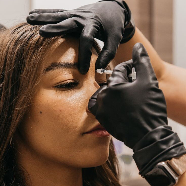 Person receiving a facial injection with gloved hands in a clinical setting