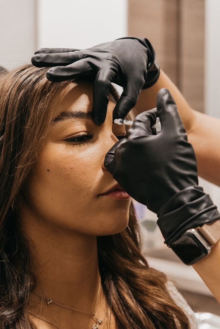 Person receiving a facial injection with gloved hands in a clinical setting