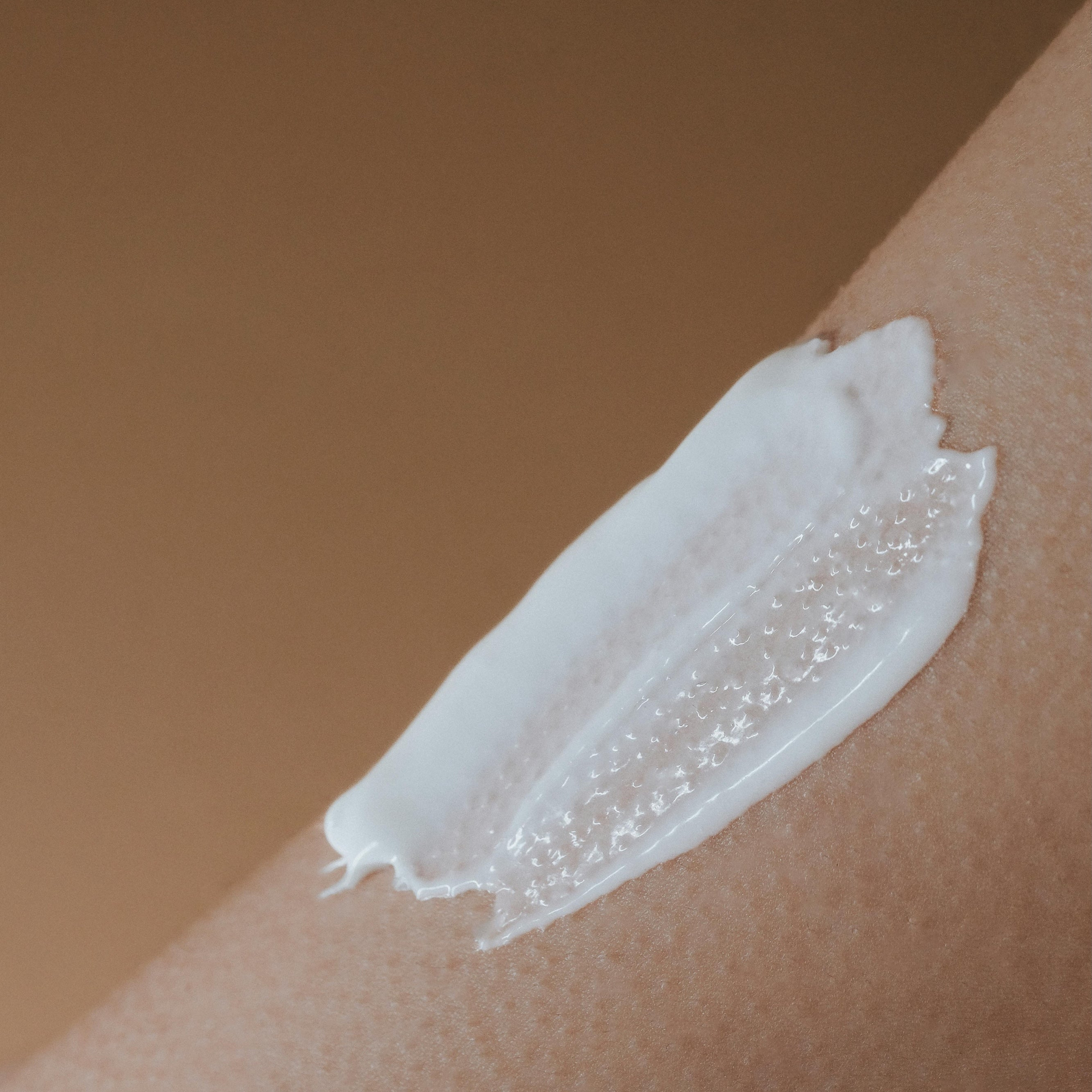 White cream or lotion applied to a person's arm against a brown background