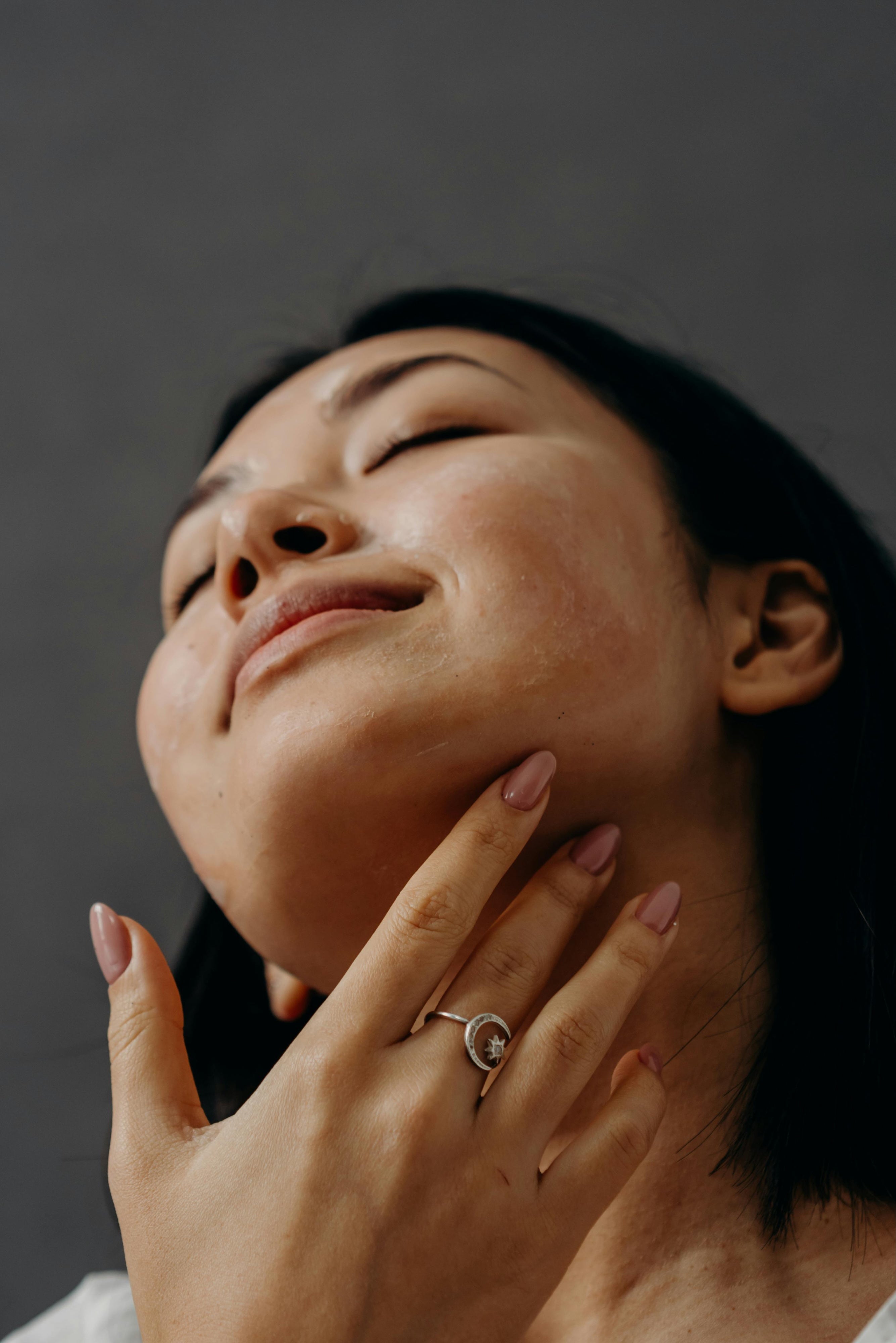 Woman with a ring on her finger touching her neck against a dark background