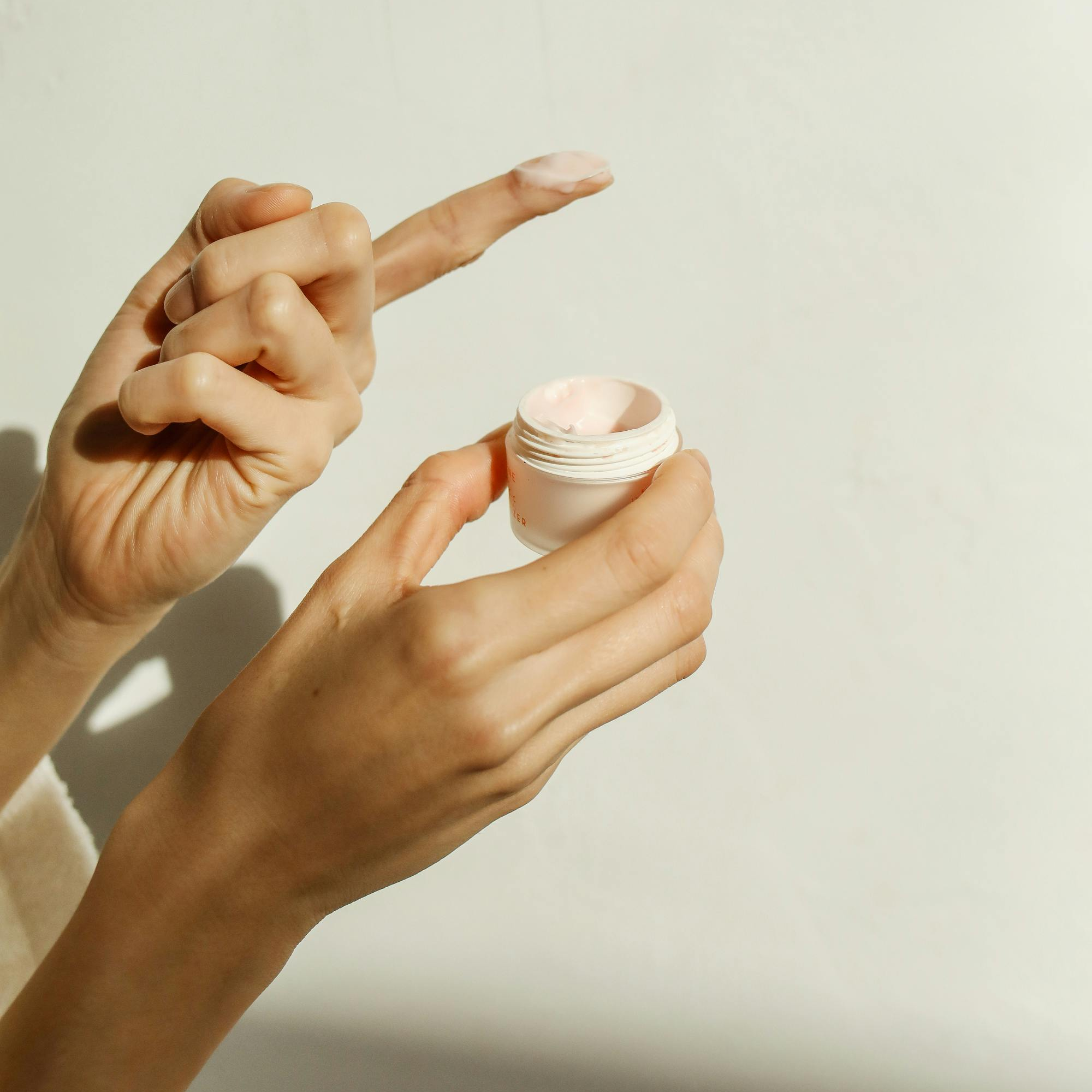 Person holding a small cosmetic container with a light-colored background