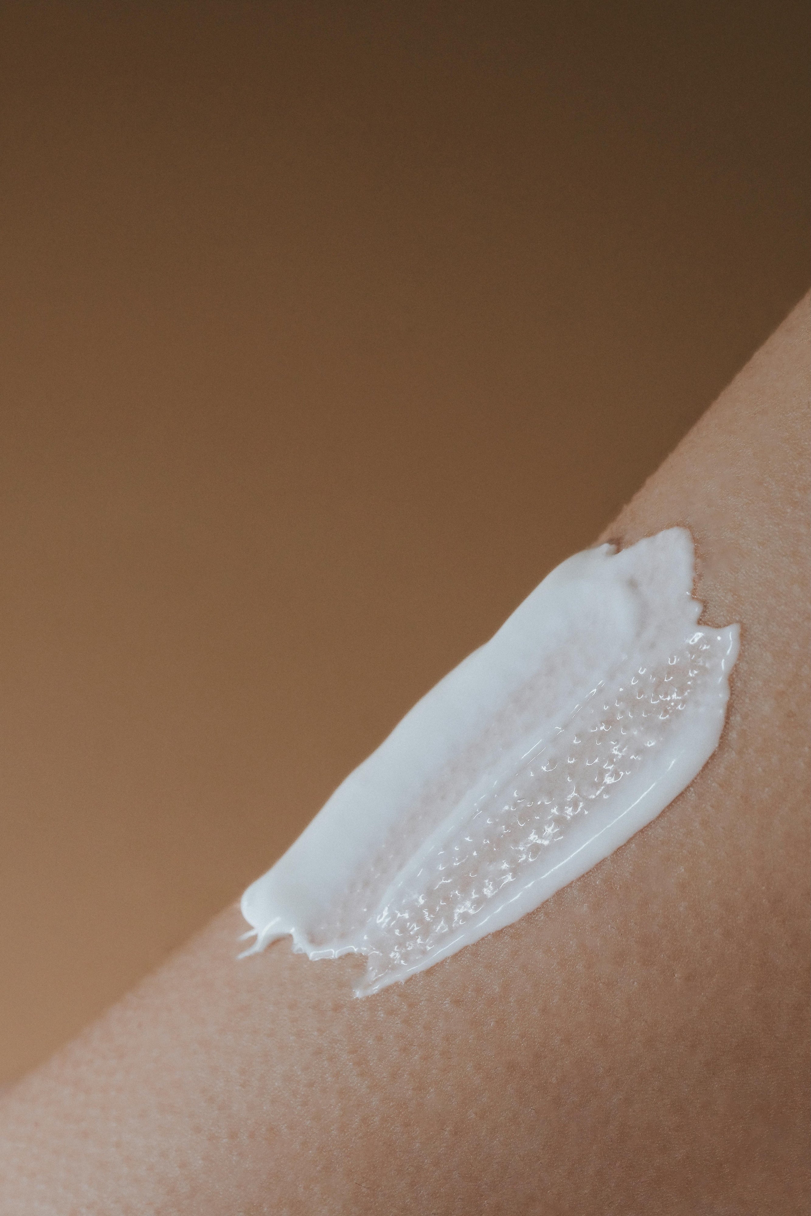 Close-up of a white lotion application on skin with a neutral background